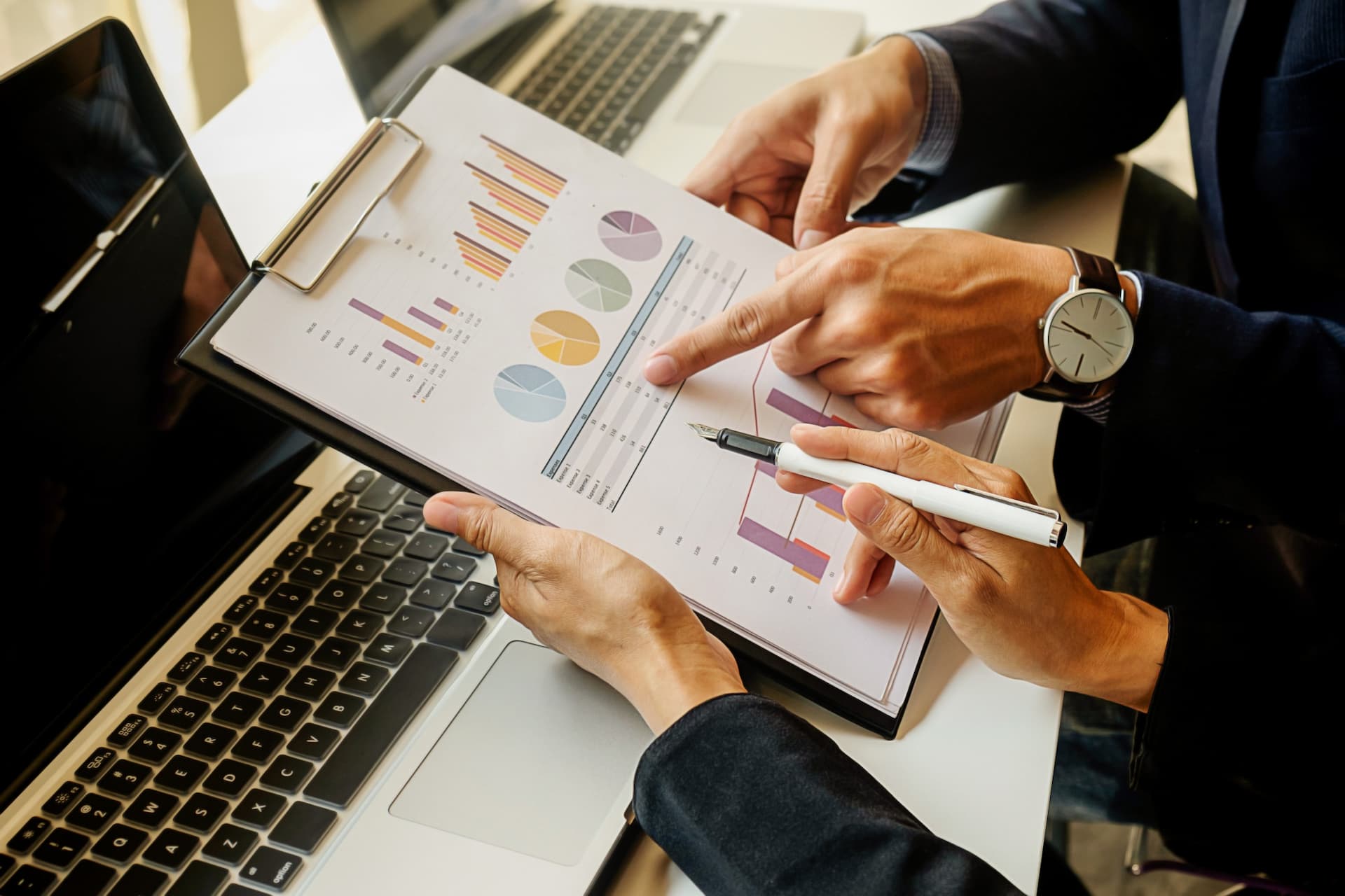Two professionals analyzing charts and graphs on a clipboard and laptop, highlighting the efficiency of job costing software for project tracking.